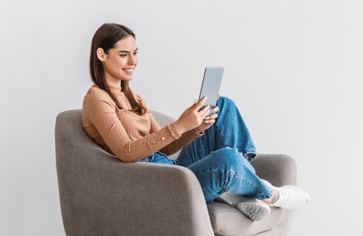 Junge Frau sitzt mit Tablet auf einem Sessel und ließt begeistert