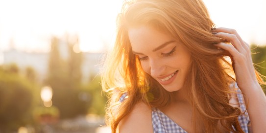 Junge Frau lächelt schüchtern mit Stadt unscharf im Hintergrund