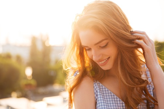 Junge Frau lächelt schüchtern mit Stadt unscharf im Hintergrund