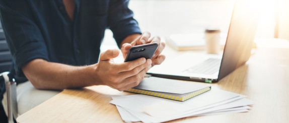 Person sitzt am Schreibtisch udn schaut etwas am Handy nach