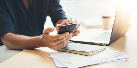 Person sitzt am Schreibtisch udn schaut etwas am Handy nach