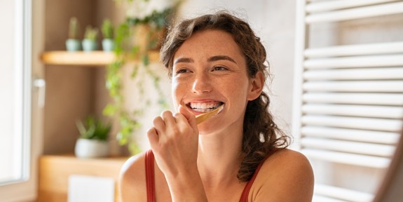 Junge Frau putzt lachend die Zähne im Spiegel