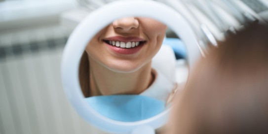 Frau bewundert ihre Zähne im Handspiegel