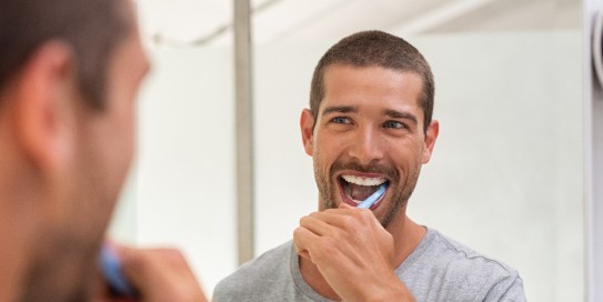 Junger Mann putzt lachend die Zähne