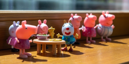Figuren aus der Serie „Peppa Wutz“ stehen aufgereiht auf einer Fensterbank, zwei von ihnen sitzen an einem kleinen Tisch mit Spielgeschirr.