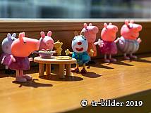 Figuren aus der Serie „Peppa Wutz“ stehen aufgereiht auf einer Fensterbank, zwei von ihnen sitzen an einem kleinen Tisch mit Spielgeschirr.