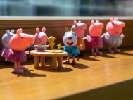 Figuren aus der Serie „Peppa Wutz“ stehen aufgereiht auf einer Fensterbank, zwei von ihnen sitzen an einem kleinen Tisch mit Spielgeschirr.