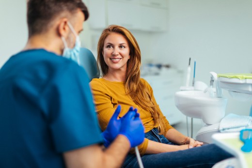 Zahnärztlicher Mitarbeiter im Gespräch mit einer Patientin auf dem Behandlungsstuhl, die lächelnd zuhört.